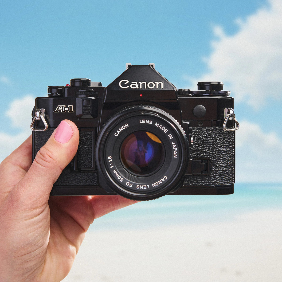 Hand holding a Canon A-1 | 35mm Film Camera against a blue sky background