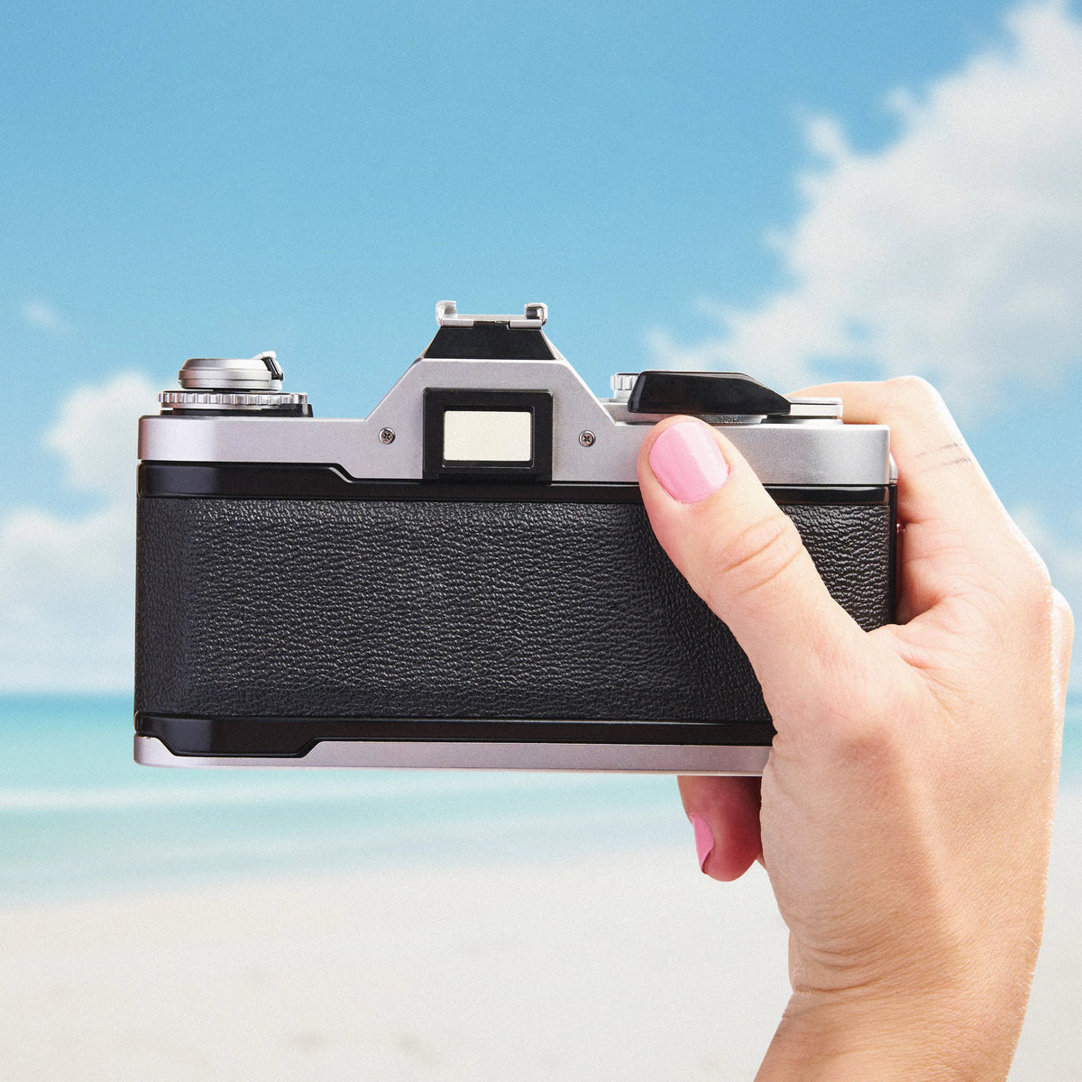 Hand holding a Canon AV-1 | 35mm Film Camera against a beach background