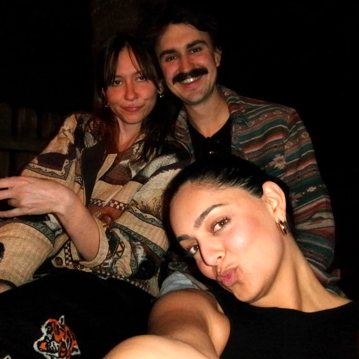 Three people posing together in a dimly lit setting