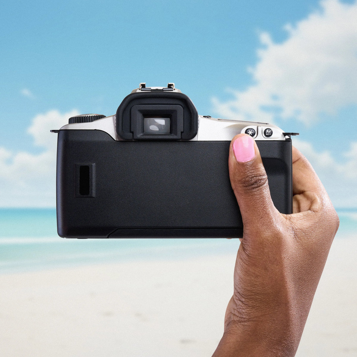 Hand holding a Canon EOS Rebel 2000 film camera with a beach and blue sky in the background