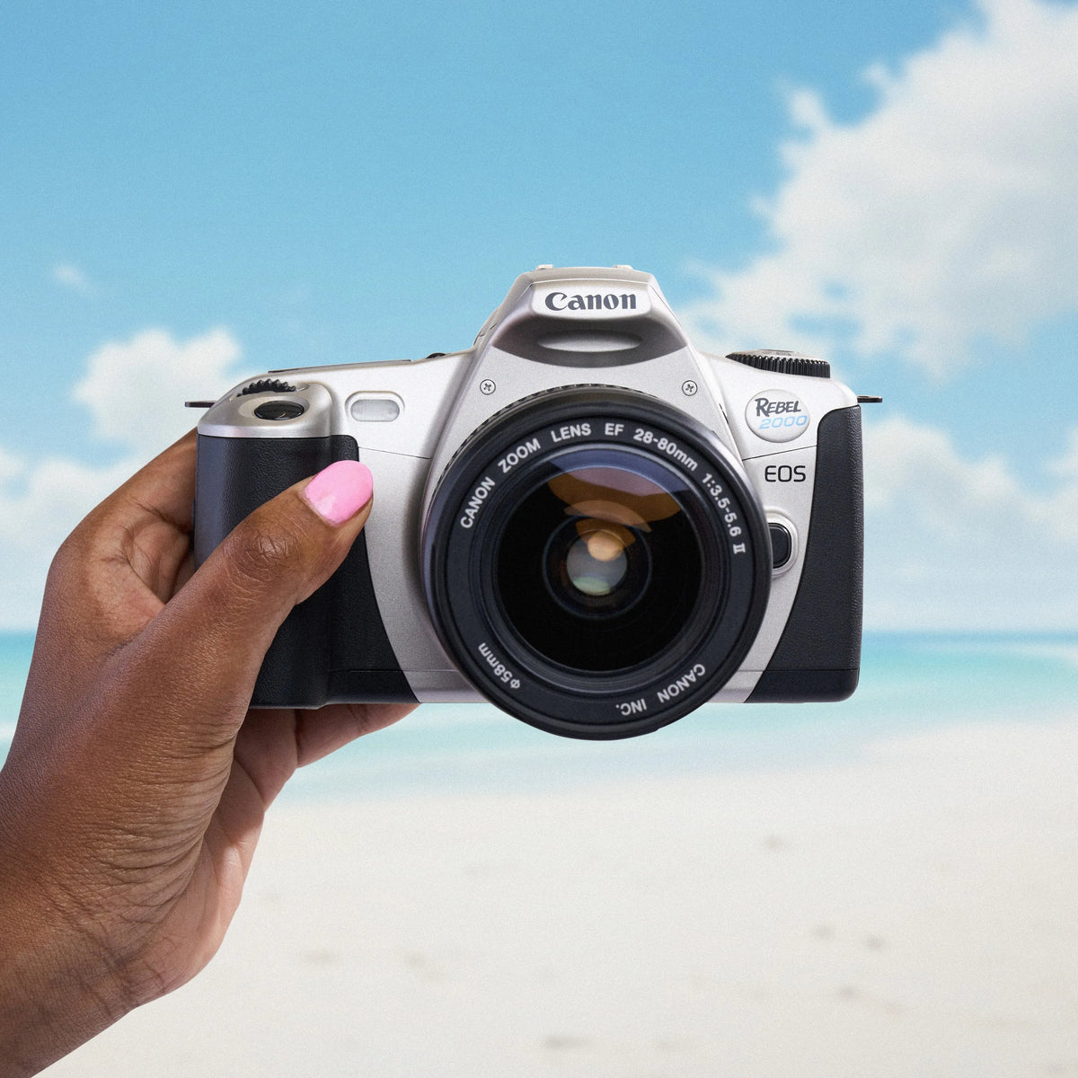 Canon EOS Rebel 2000 film camera held by a hand with a beach and sky background