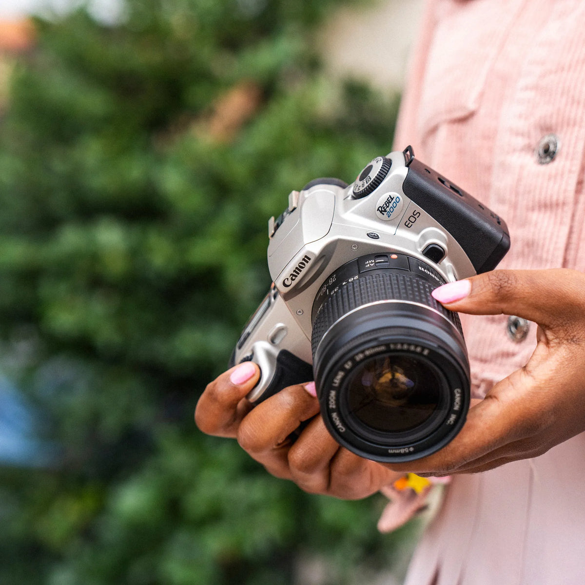 Person holding a Canon EOS Rebel 2000 film camera with a blurred green background