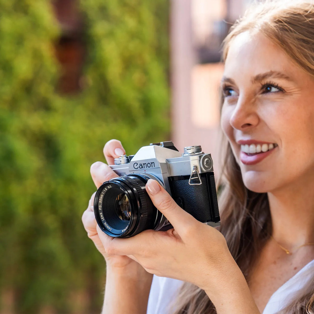 Woman holding a Canon FTB 35mm film camera with a blurred green background