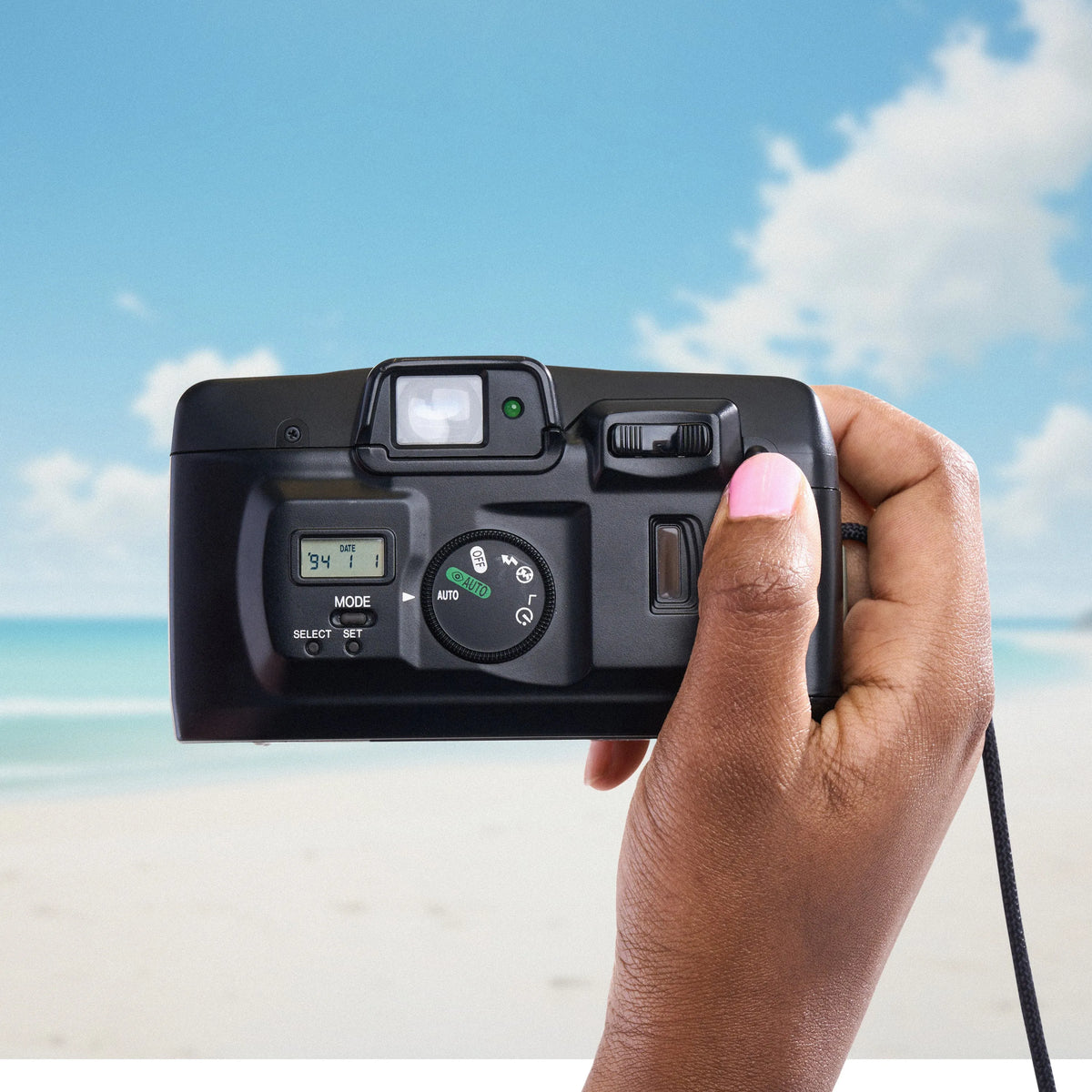 Hand holding a Canon Sure Shot 60 Zoom 35mm Camera with a beach and blue sky in the background