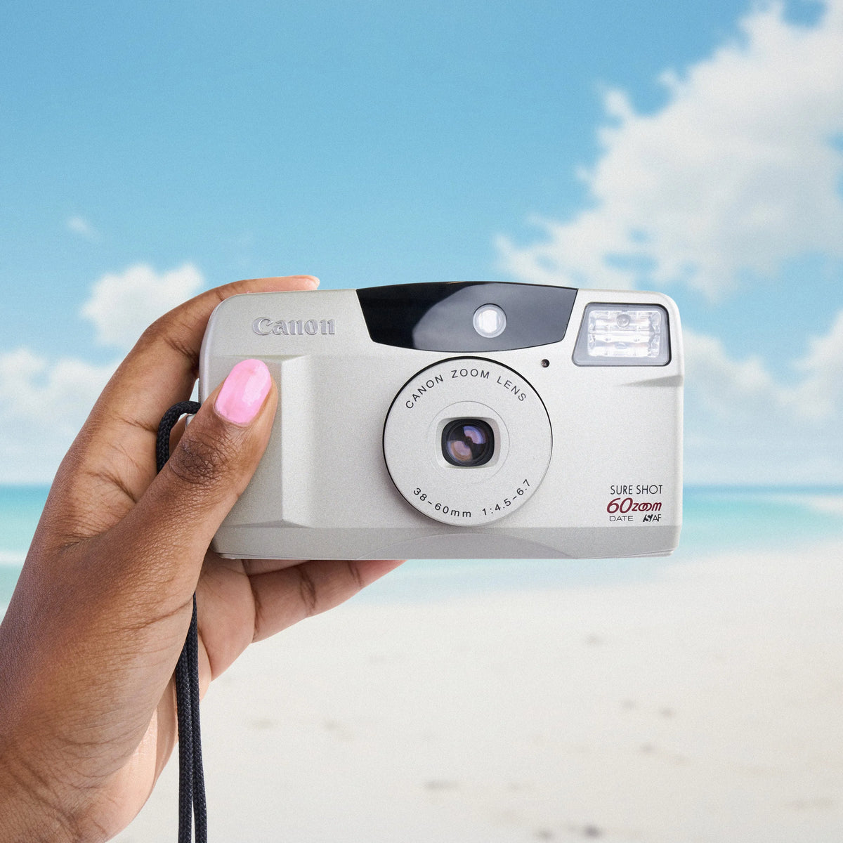 Hand holding a Canon Sure Shot 60 Zoom 35mm Camera with a beach and blue sky in the background