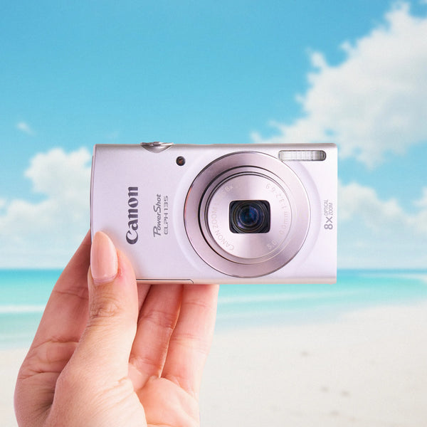 Canon Powershot ELPH 135 camera held in a hand with a beach background