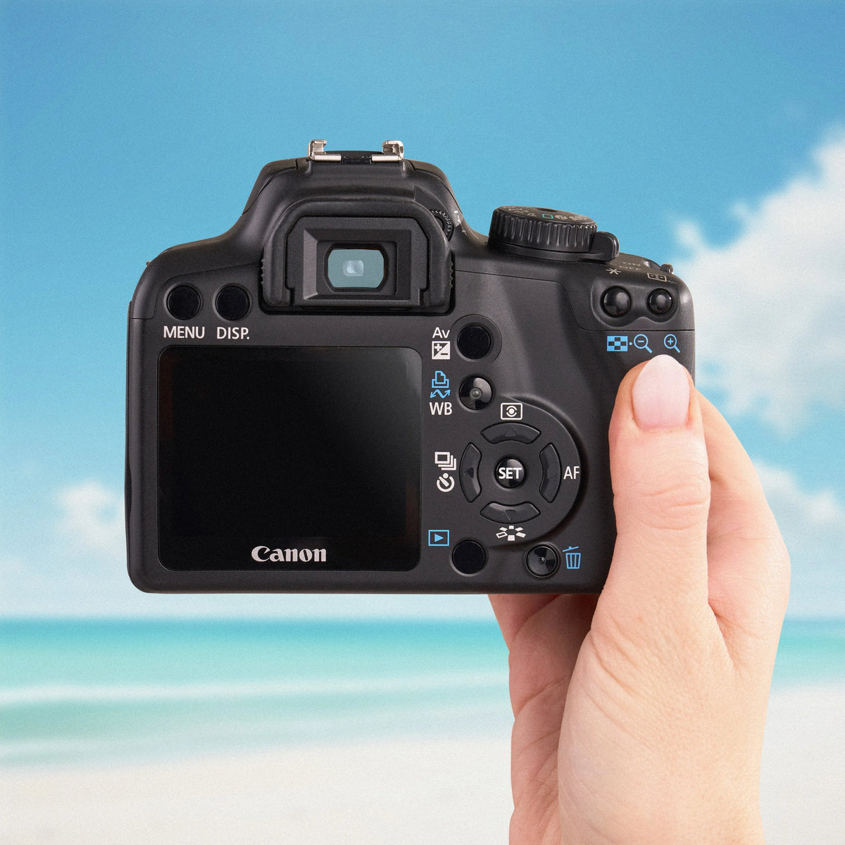 Canon Rebel XS held in a hand with a beach background