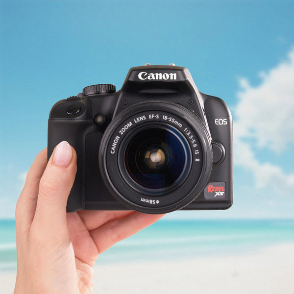 Canon Rebel XS held in a hand with a beach background