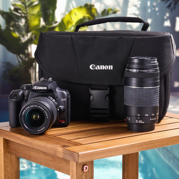 Canon camera and lenses on a wooden table with a pool and plants in the background