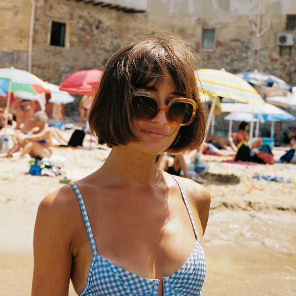 Woman on a beach wearing sunglasses and a blue checkered dress with people and umbrellas in the background. taken with the Contax G1 Rangefinder Film Camera
