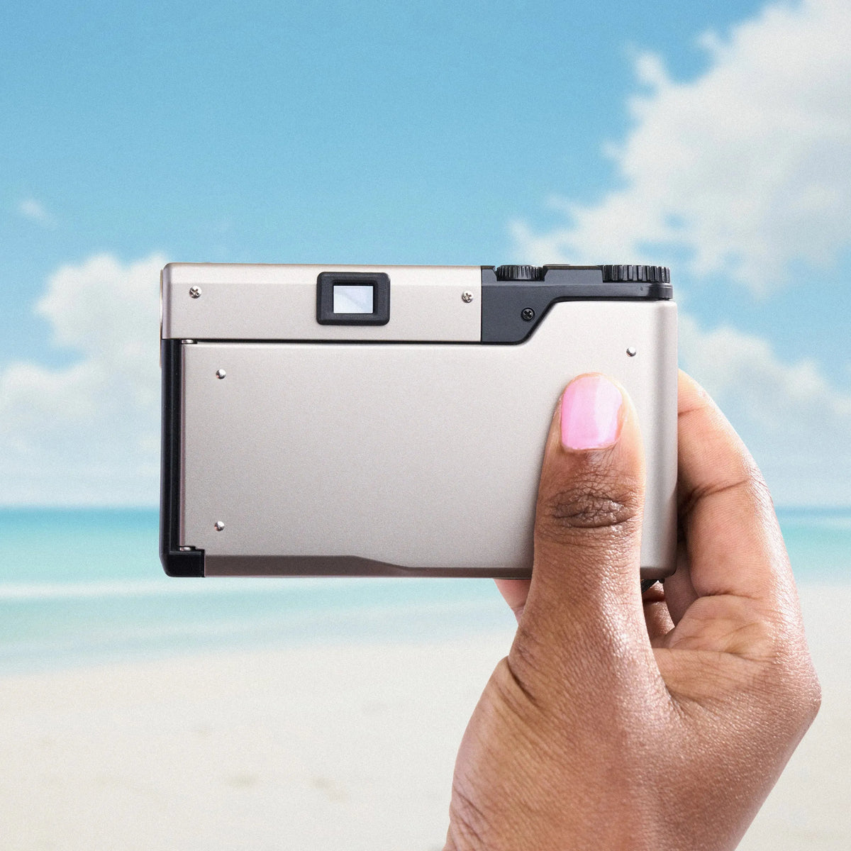 Hand holding a silver Contax T3 35mm Point and Shoot Camera against a beach background