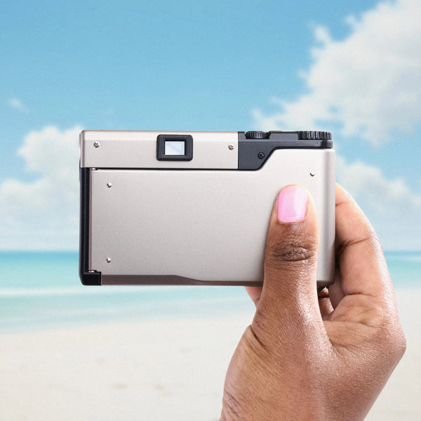 Hand holding a silver Contax T3 35mm Point and Shoot Camera against a beach background