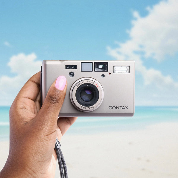 Hand holding a Contax T3 35mm Point and Shoot Camera with a beach and sky background