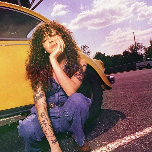 Woman with curly hair and tattoos sitting on a yellow car in a parking lot taken with the Nikon FM2 Film Camera