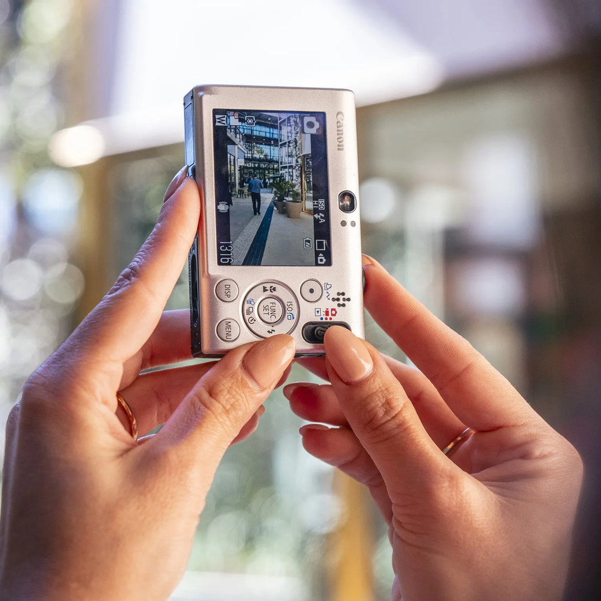 Person holding a Canon PowerShot ELPH SD1100 IS taking a photo of a street scene