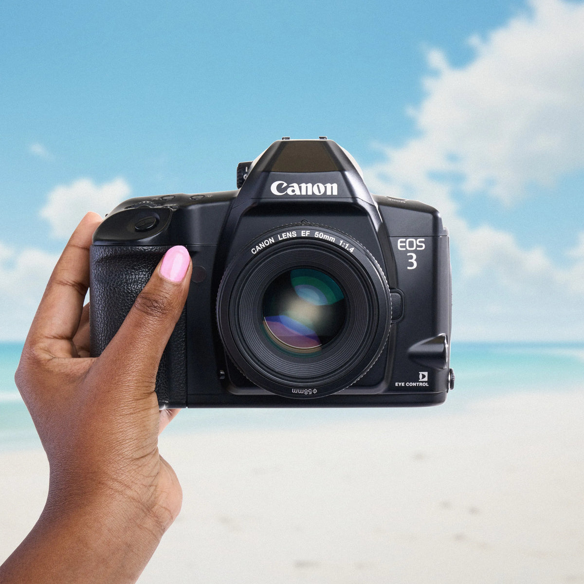 Canon EOS 3 camera held by a hand with a beach background