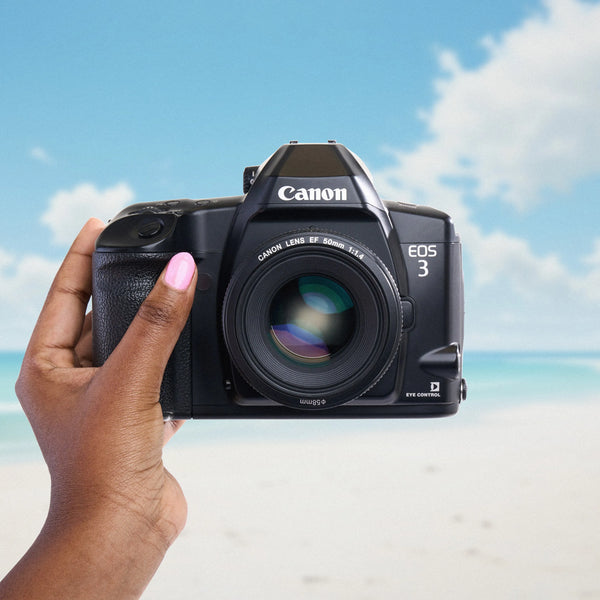 Canon EOS 3 camera held by a hand with a beach background