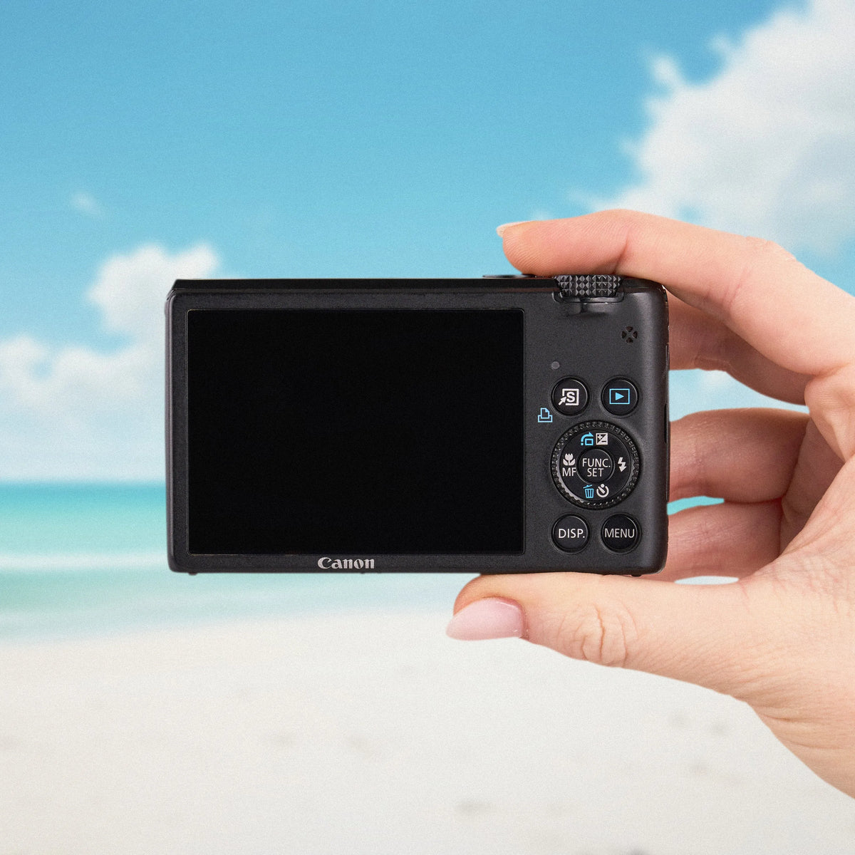 Back view of the Canon PowerShot S95 showing its LCD screen and controls against a beach backdrop