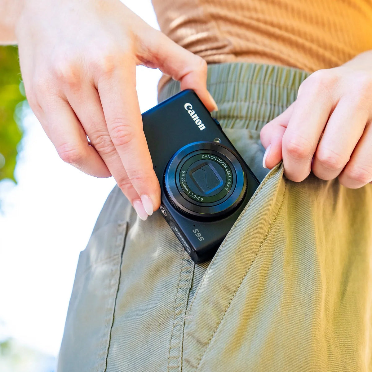 Canon PowerShot S95 compact camera being placed into a pants pocket