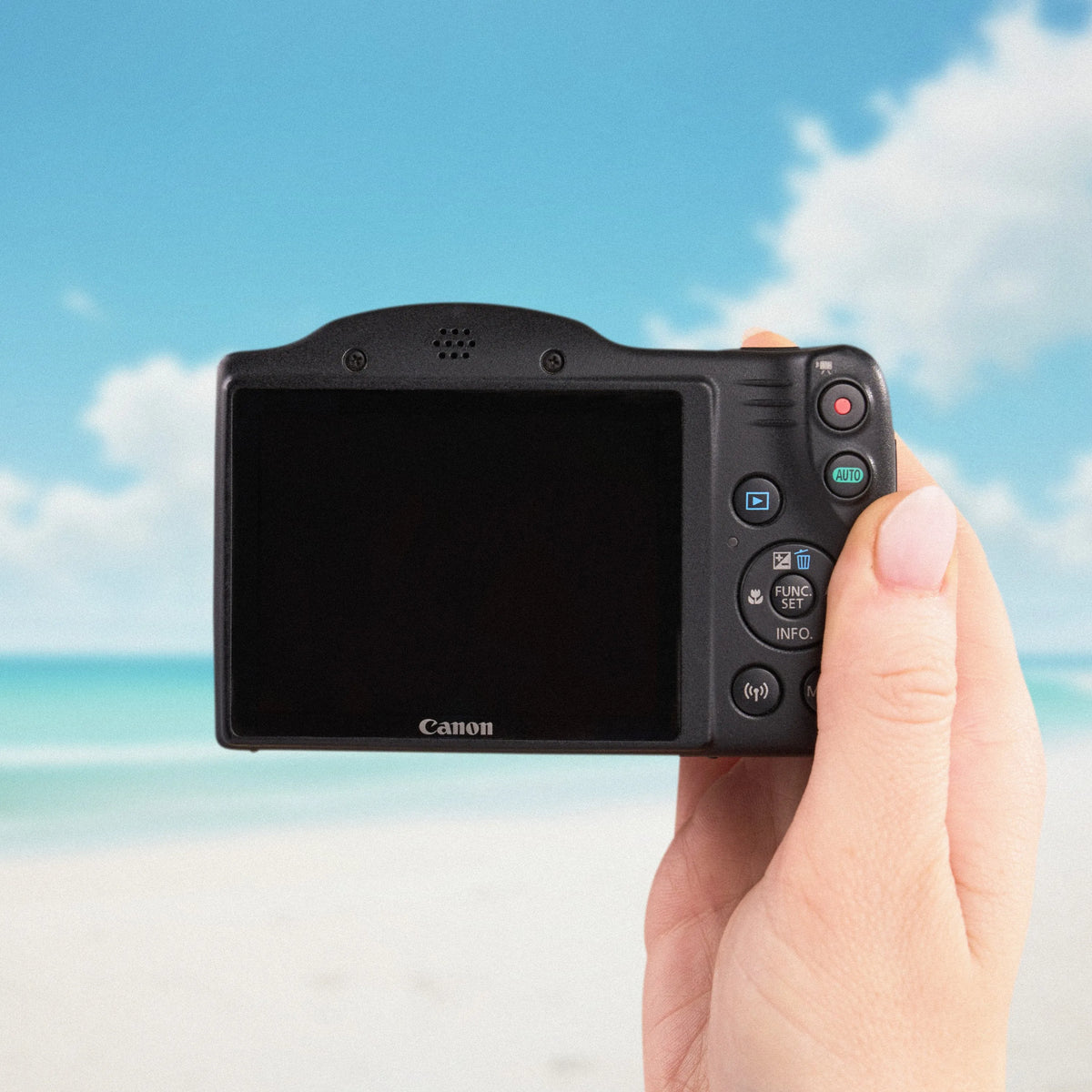 Back view of the Canon PowerShot SX420 IS showing its LCD screen and controls against a beach backdrop