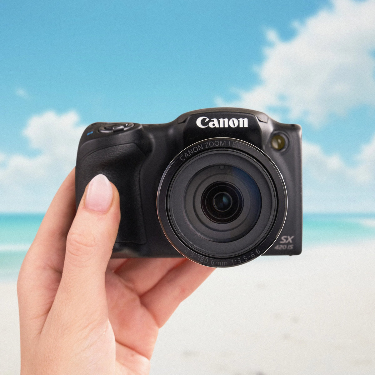 Canon PowerShot SX420 IS held from the front against a beach backdrop