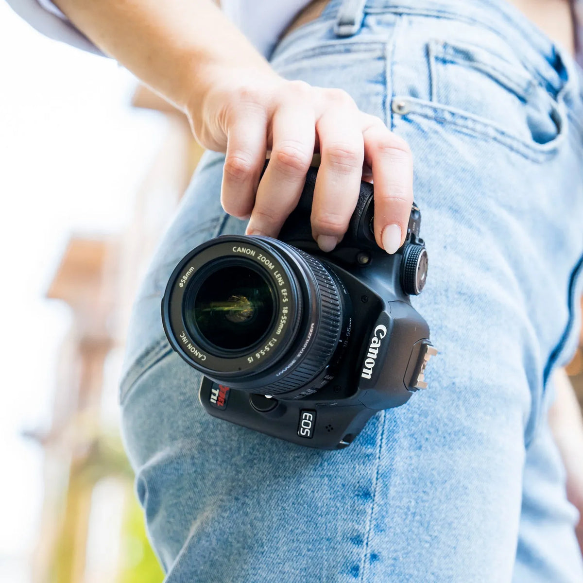 Canon Rebel T1i DSLR camera carried by its grip beside a pair of jeans