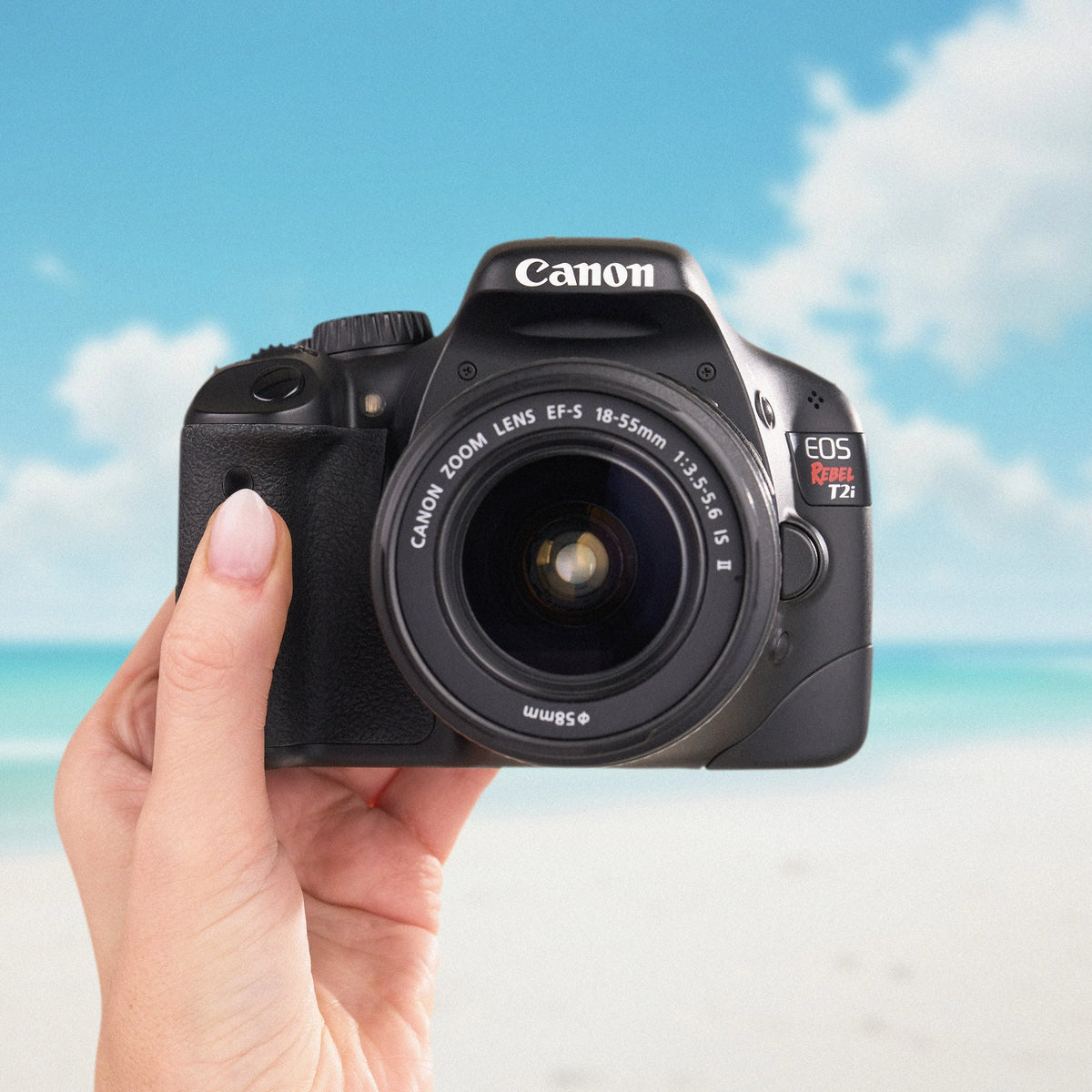 Canon Rebel T2i DSLR camera with an 18–55mm lens held against a beach backdrop