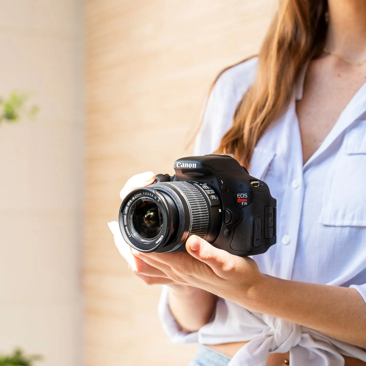 Woman holding a Canon Rebel T3i DSLR camera with an 18–55mm lens indoors