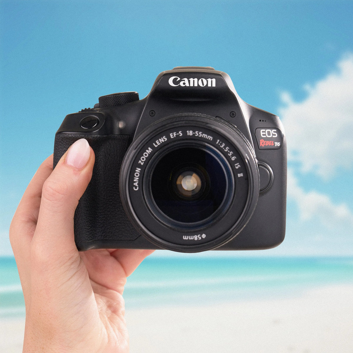Canon Rebel T6 DSLR Camera held in a hand with a beach background