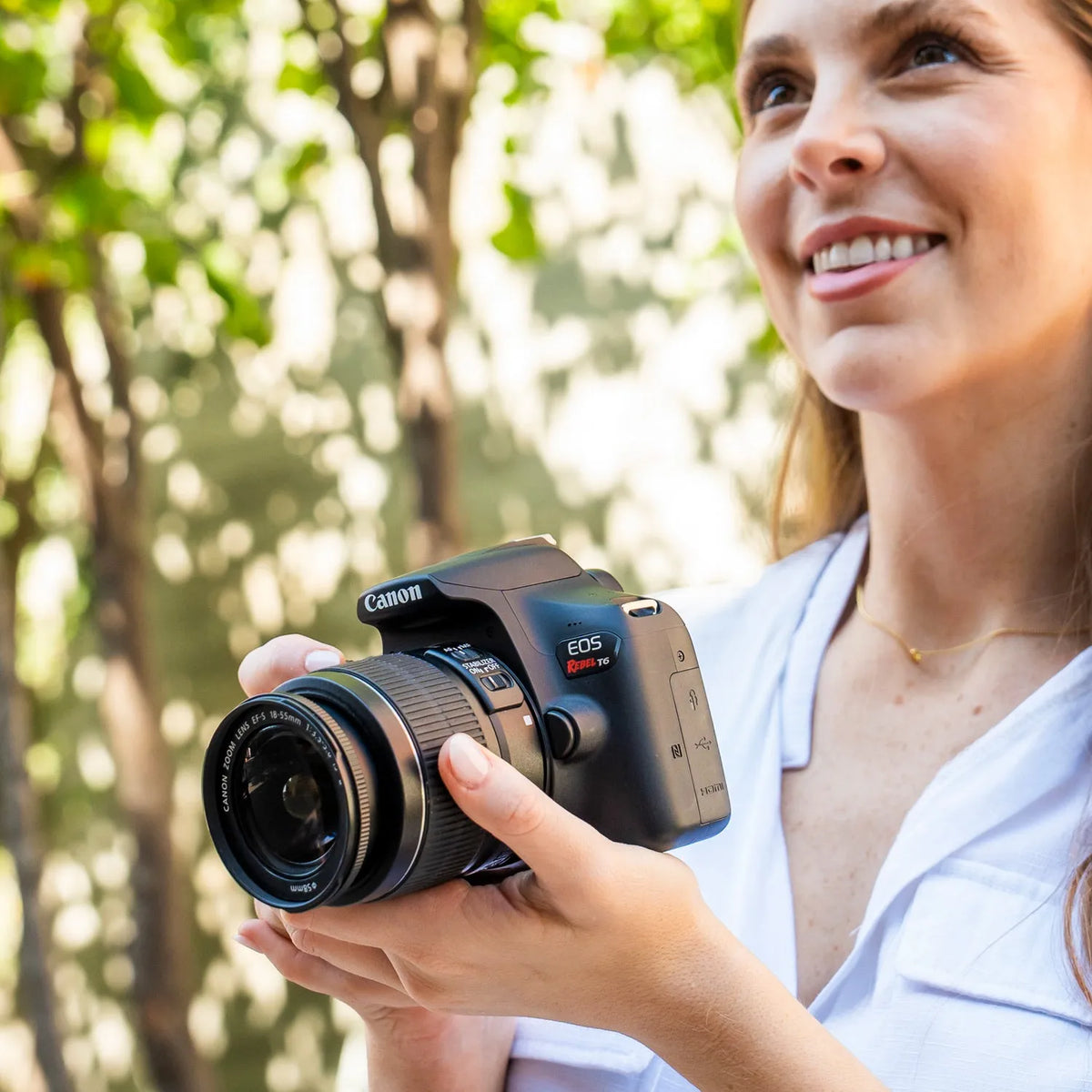 Woman holding a Canon camera outdoors with greenery in the background