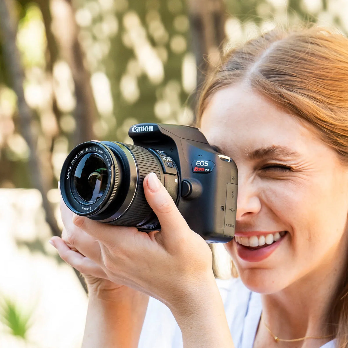 Woman holding a Canon Rebel T6 DSLR Camera outdoors with a blurred natural background