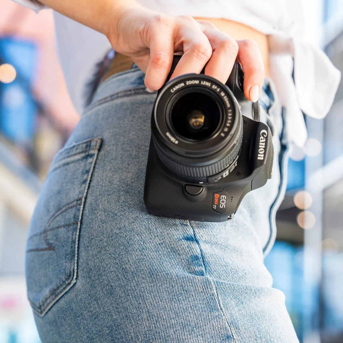 Canon Rebel T7 DSLR camera carried by its grip beside a pair of jeans