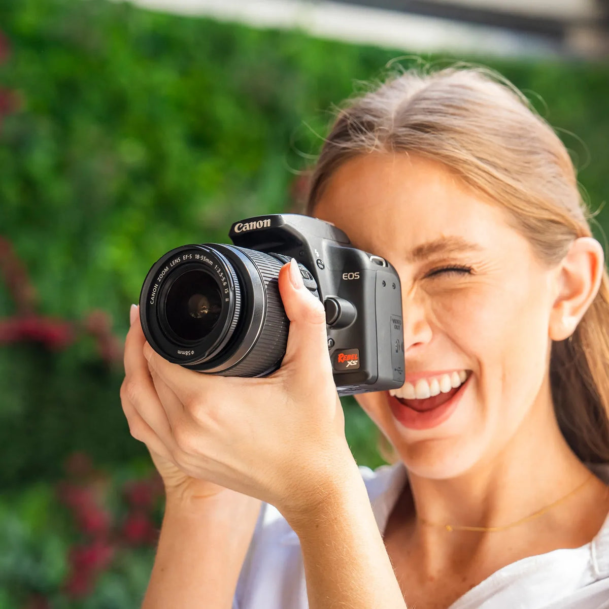 Woman holding a Canon Rebel XS with a blurred green background