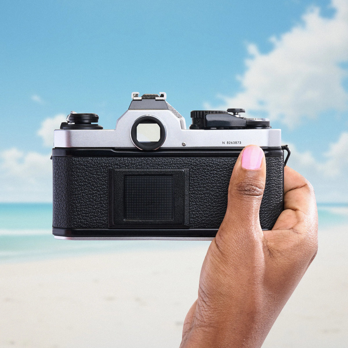 Hand holding a Nikon FM2 Film Camera with a beach and blue sky in the background