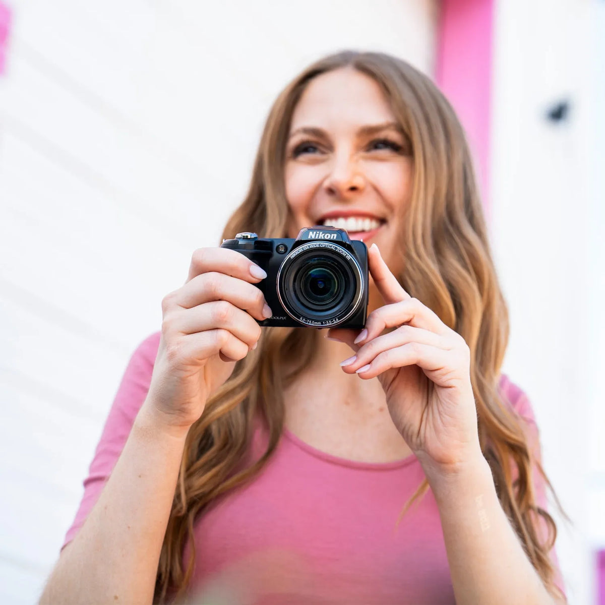 Woman smiling while holding a Nikon COOLPIX L110 retro digital camera