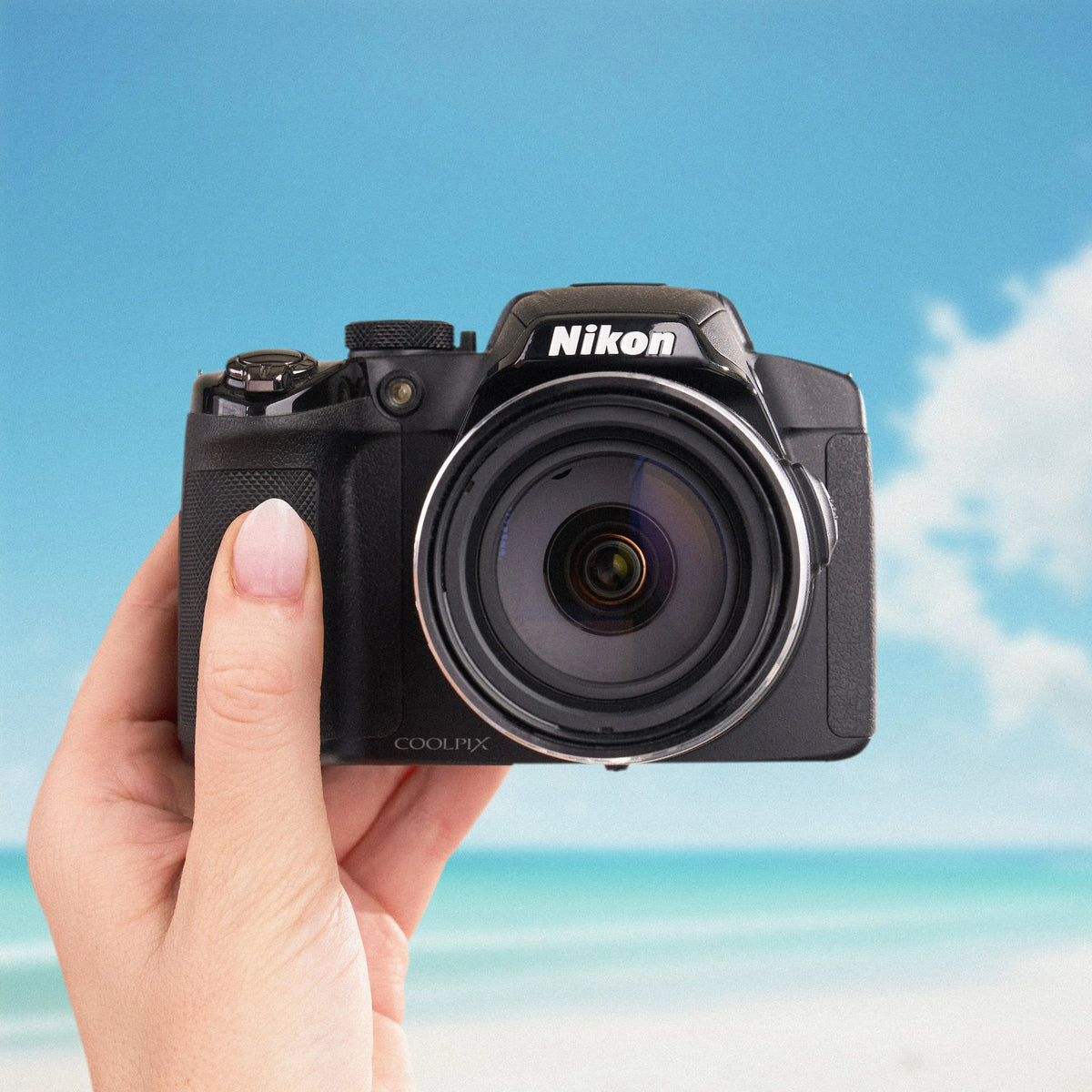 Front view of a black Nikon COOLPIX P510 held against a sunny beach background