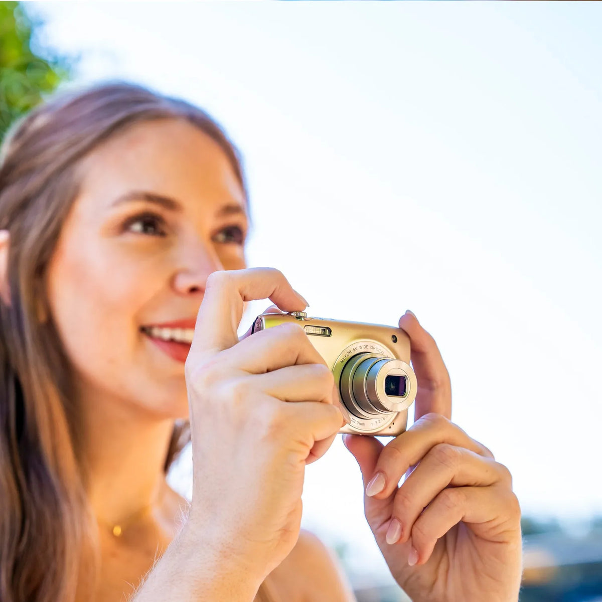 Woman smiling while taking a photograph outdoors with a silver Nikon COOLPIX S3300