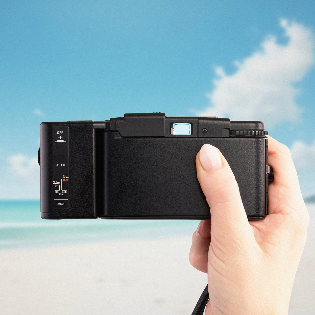 Hand holding a Olympus XA 2 | 35mm Point and Shoot Film Camera against a beach background