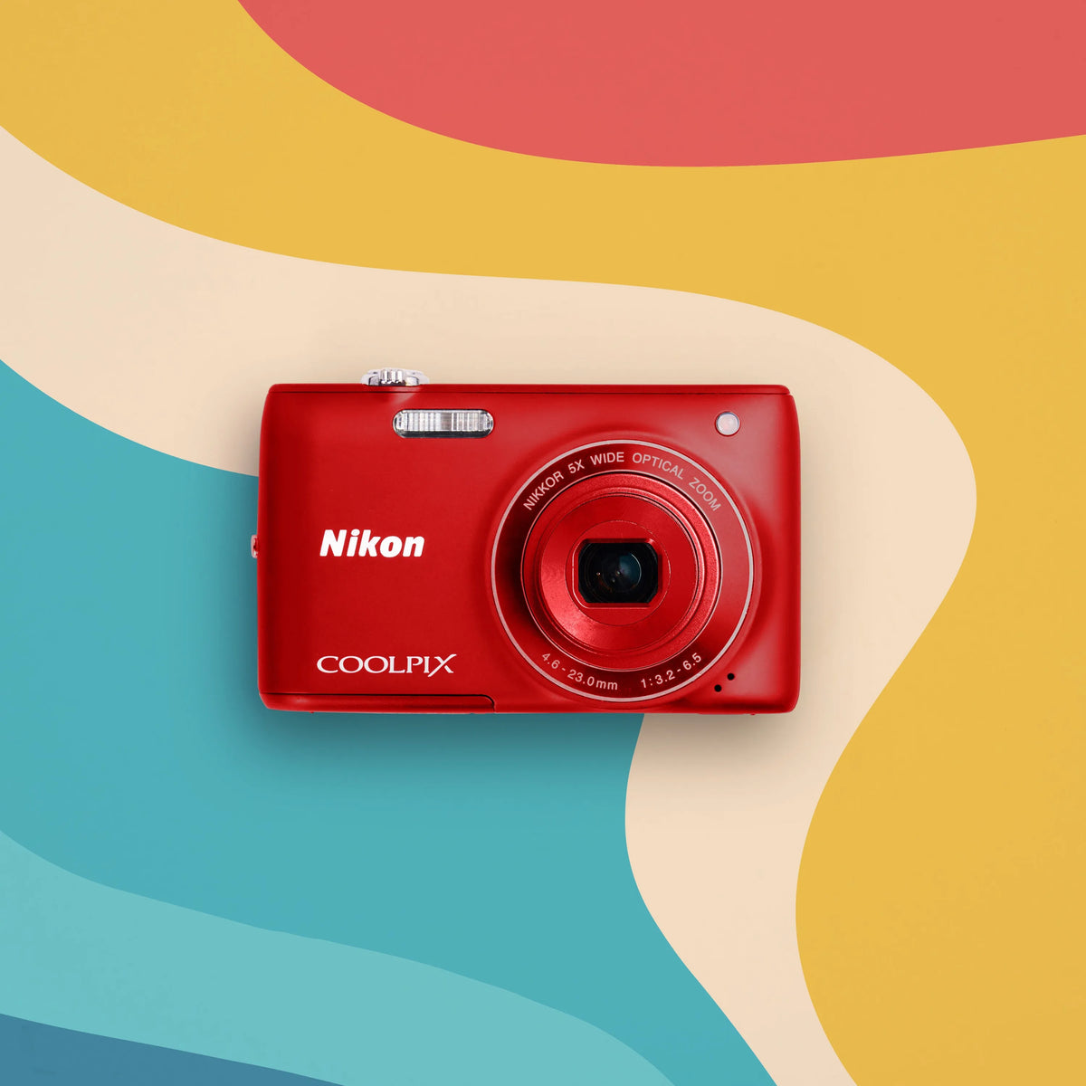 Red Nikon Coolpix S4100 retro digital camera on a colorful wavy background