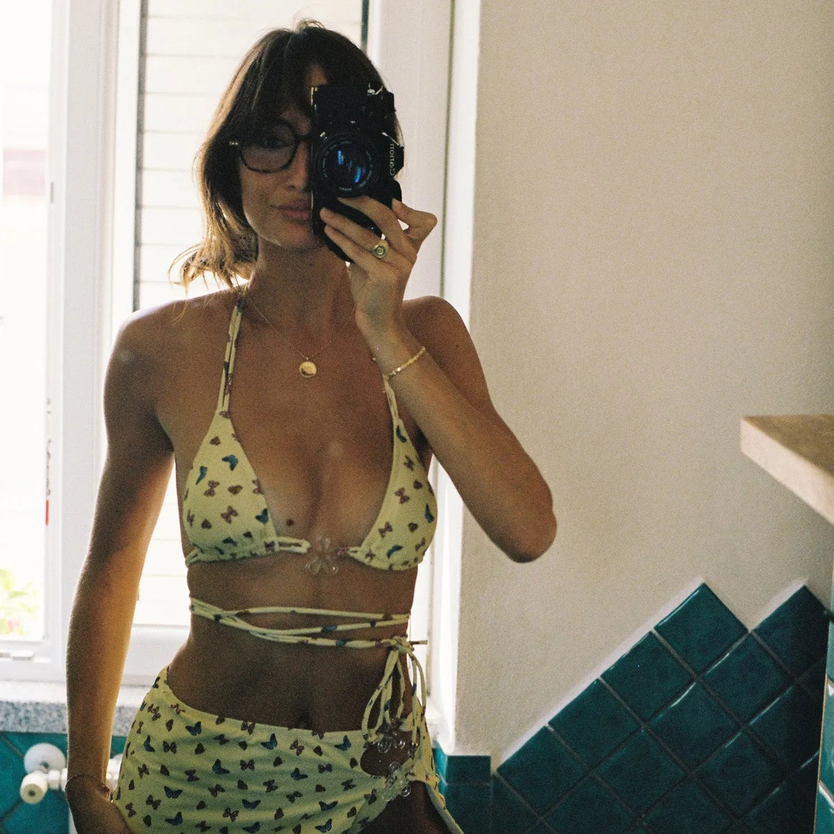 Woman taking a mirror selfie with a Canon A-1 | 35mm Film Camera wearing a yellow patterned bikini.