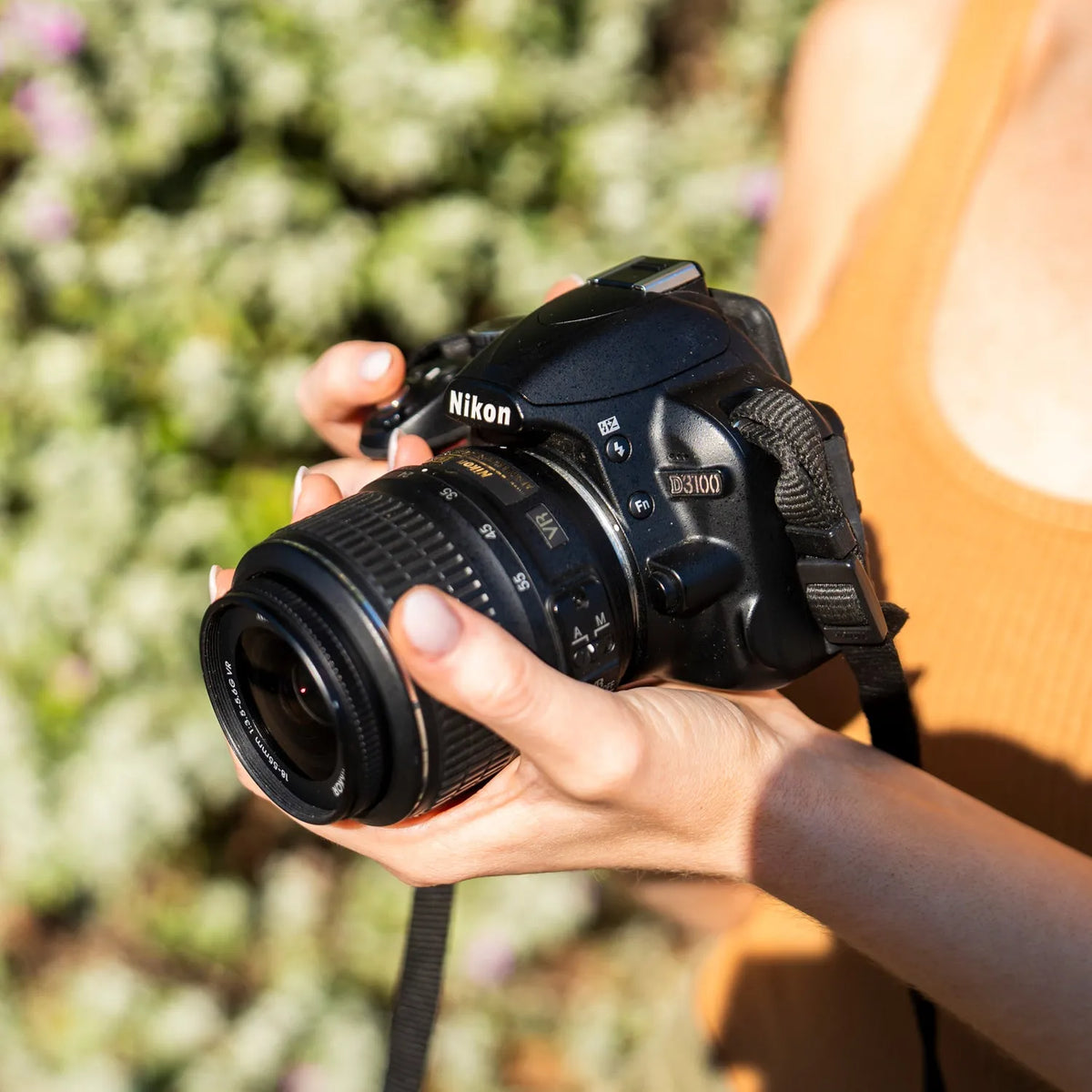 Close-up of a woman holding a Nikon D3100 DSLR camera outdoors