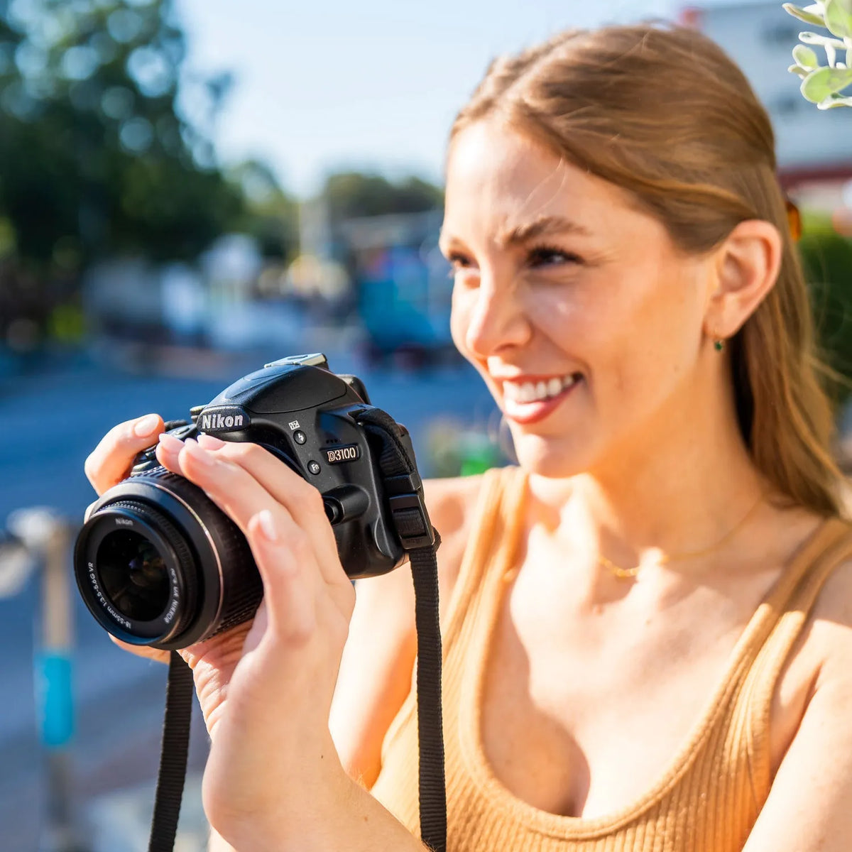 Woman smiling while taking a photograph outdoors with a Nikon D3100 DSLR