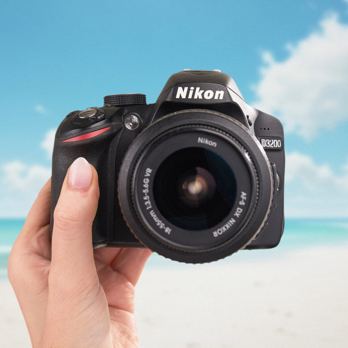 Nikon D3200 DSLR Camera held in a hand with a beach background