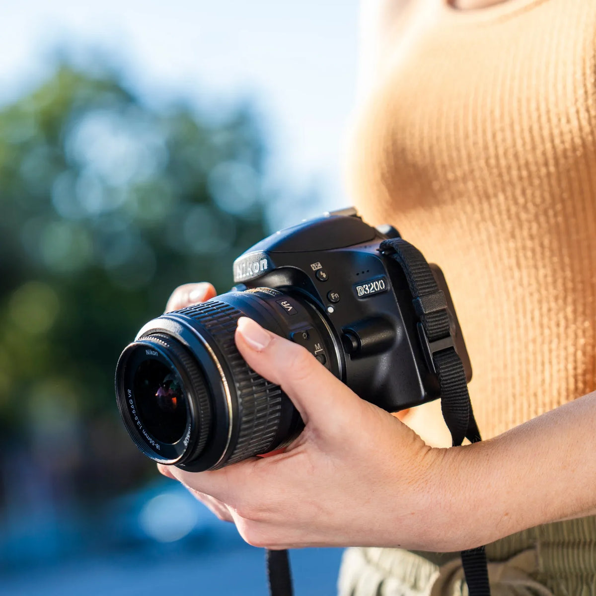 Person holding a Nikon D3200 DSLR Camera with a blurred natural background