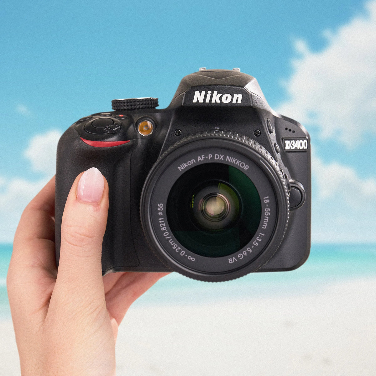 Front view of a Nikon D3400 DSLR camera held against a sunny beach background