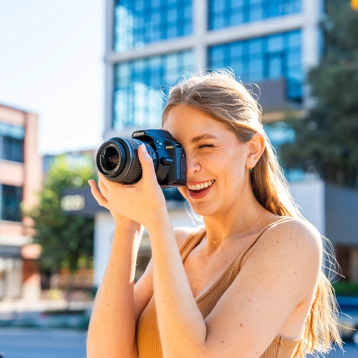 Woman smiling while taking a photograph outdoors with a Nikon D3400 DSLR camera