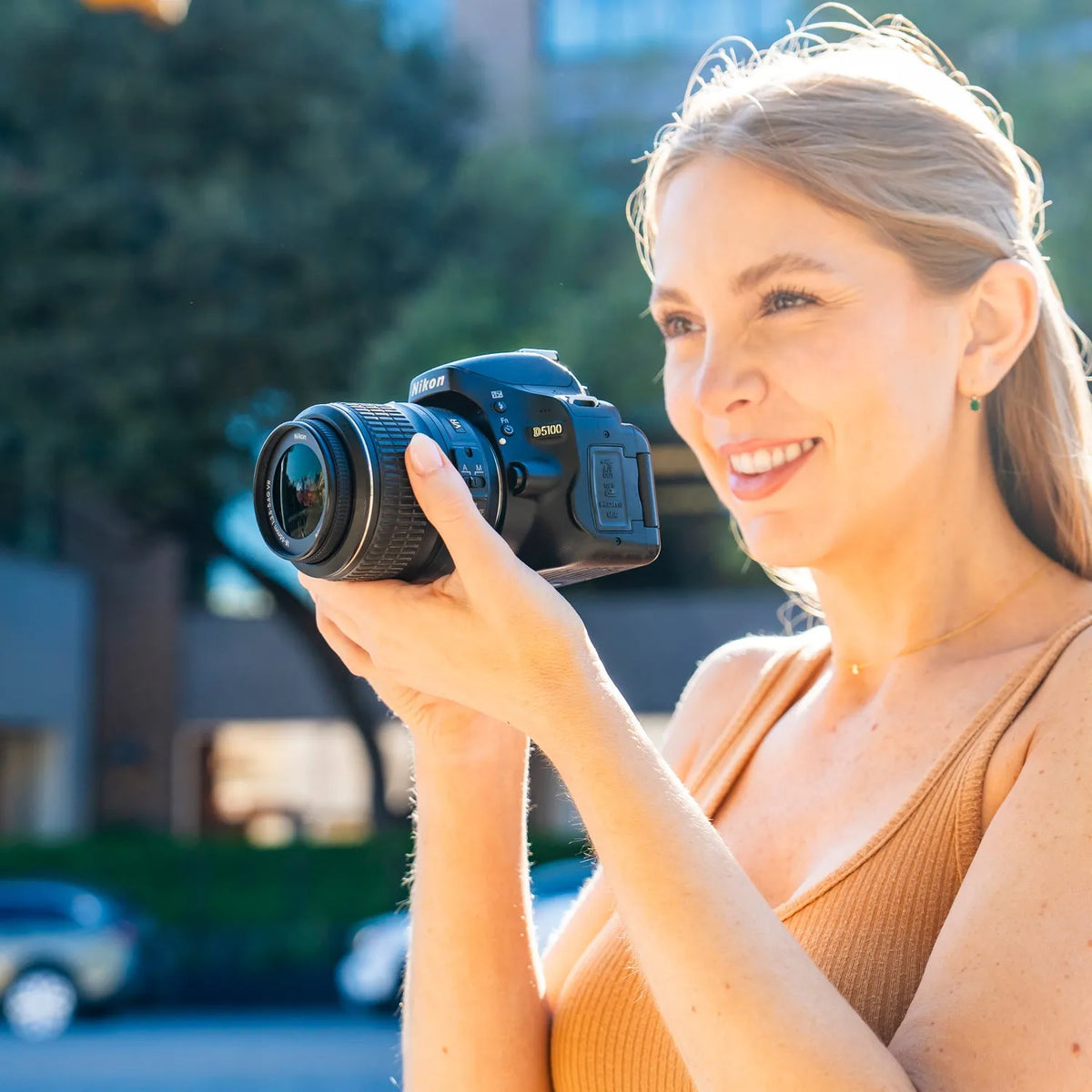 Woman using a Nikon D5100 DSLR camera with a zoom lens outdoors