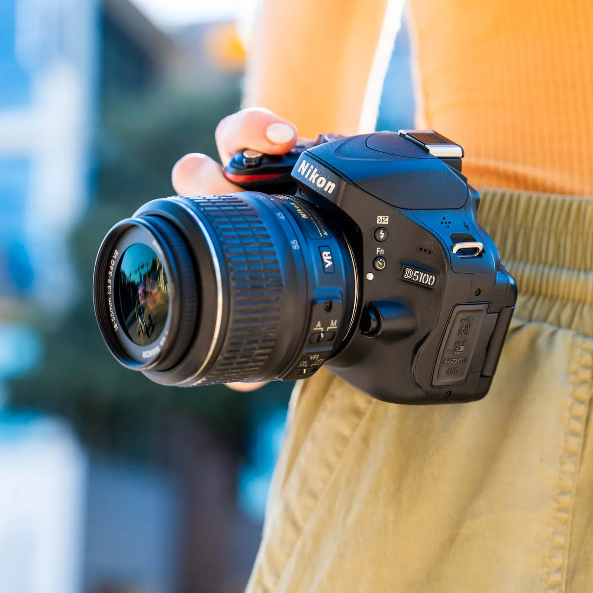 Close-up of a Nikon D5100 DSLR camera with a zoom lens held outdoors