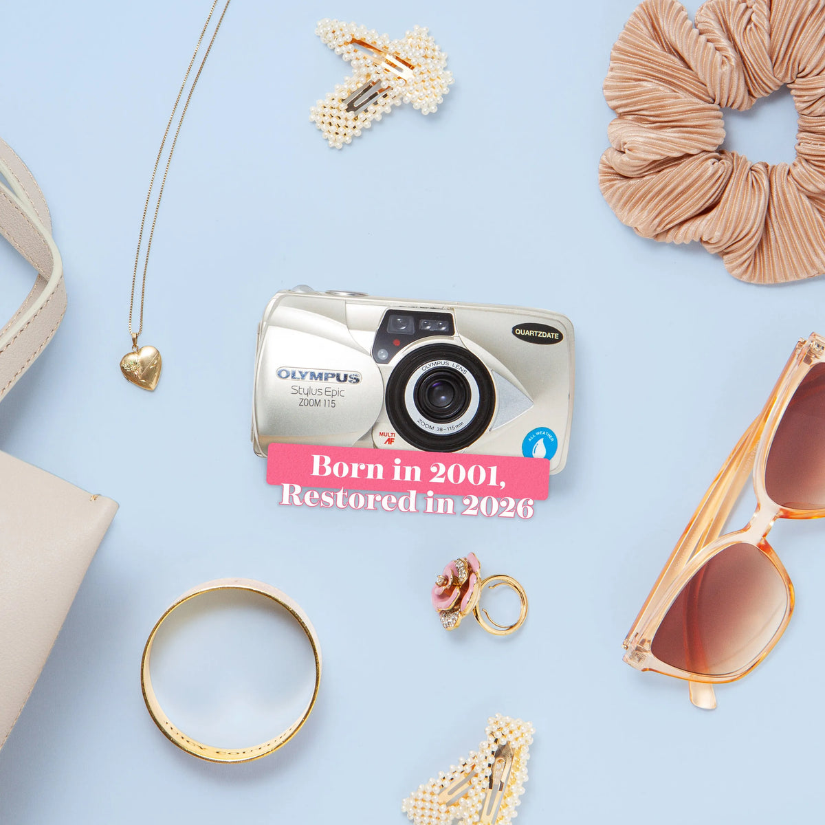 Olympus camera surrounded by accessories on a light blue background