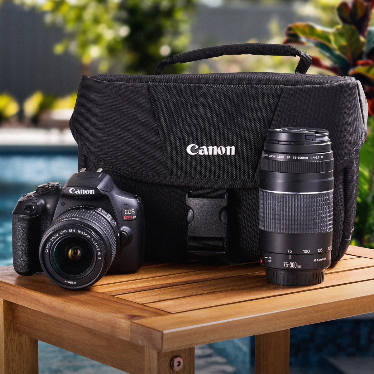 Canon Rebel T6 DSLR Camera with lenses and bag on a wooden table outdoors